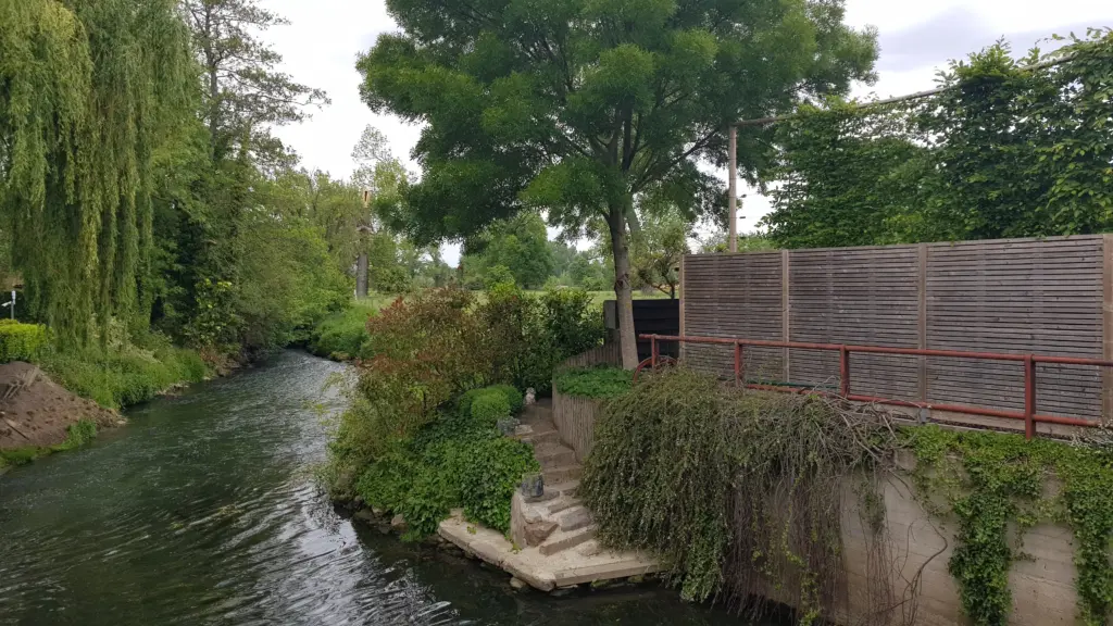 Il fiume Geer che scorre tra giardini privati e salici piangenti, con una scalinata in pietra sulla riva, presso il confine tra Kanne e Maastricht