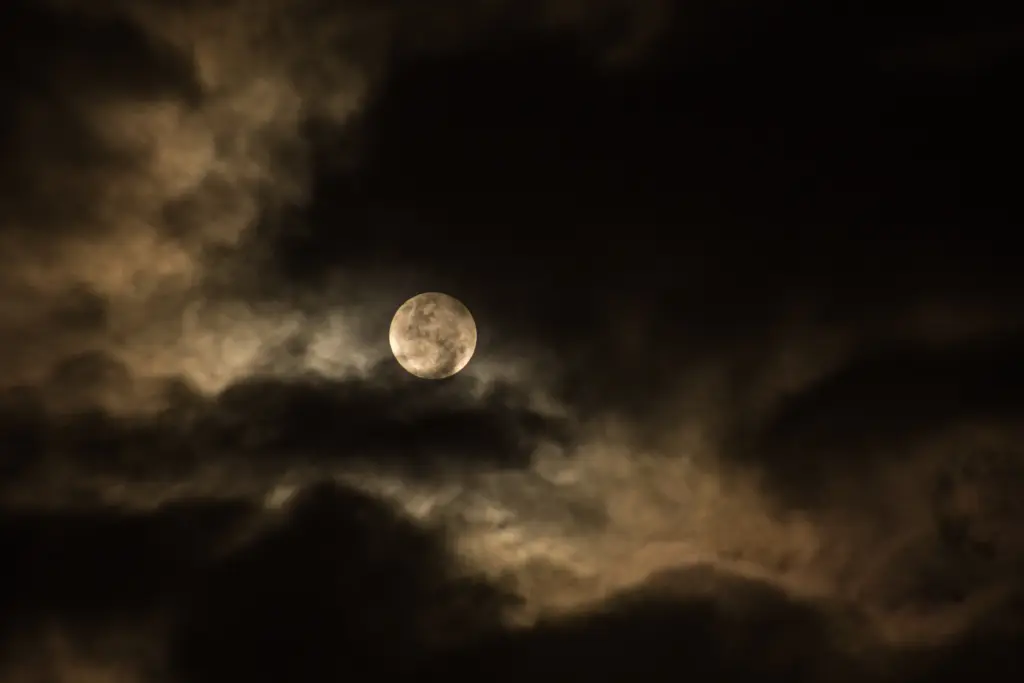 Luna piena parzialmente velata da nuvole dense in un cielo notturno