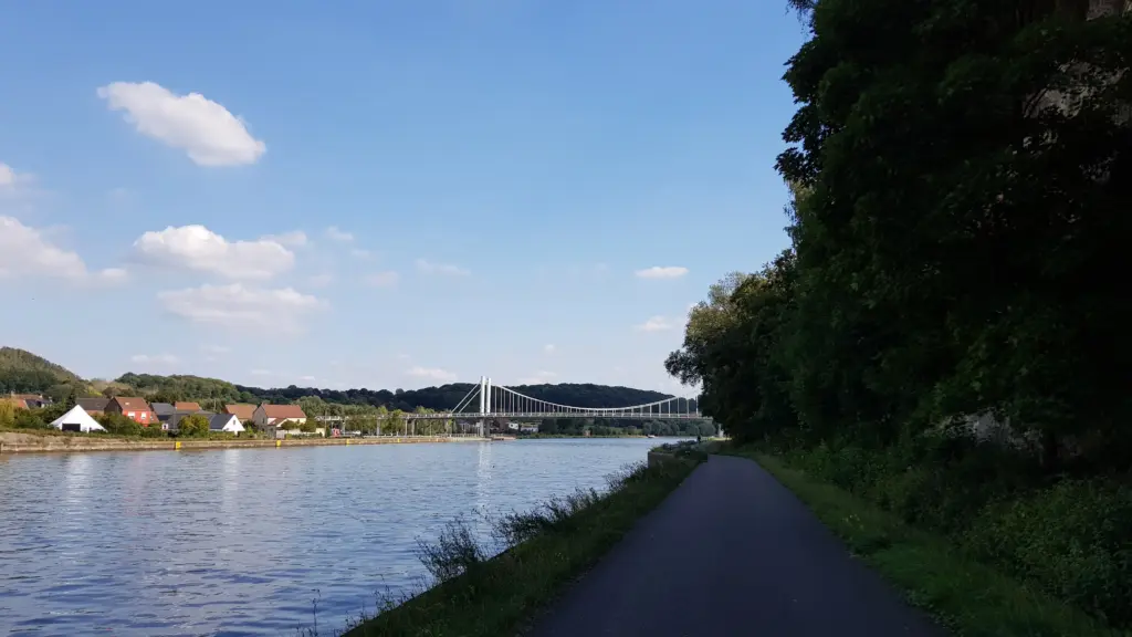 Pista ciclabile lungo il canale Albert a Kanne, con il ponte sospeso e il villaggio sullo sfondo in una giornata di sole
