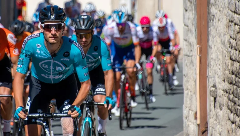 Gruppo di ciclisti professionisti in gara lungo una strada, con un corridore in primo piano e il plotone alle sue spalle.
