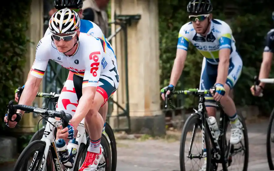 Due ciclisti professionisti affrontano un tratto di strada durante una gara, con un corridore della Lotto in primo piano